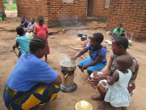 Judith boiling tea to feed family members. Glory (CHW Volunteer) is speaking to her